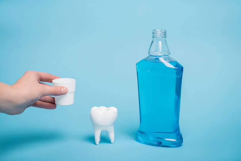 woman holding a cap near a tooth model and a bottle of mouthwash on a blue background